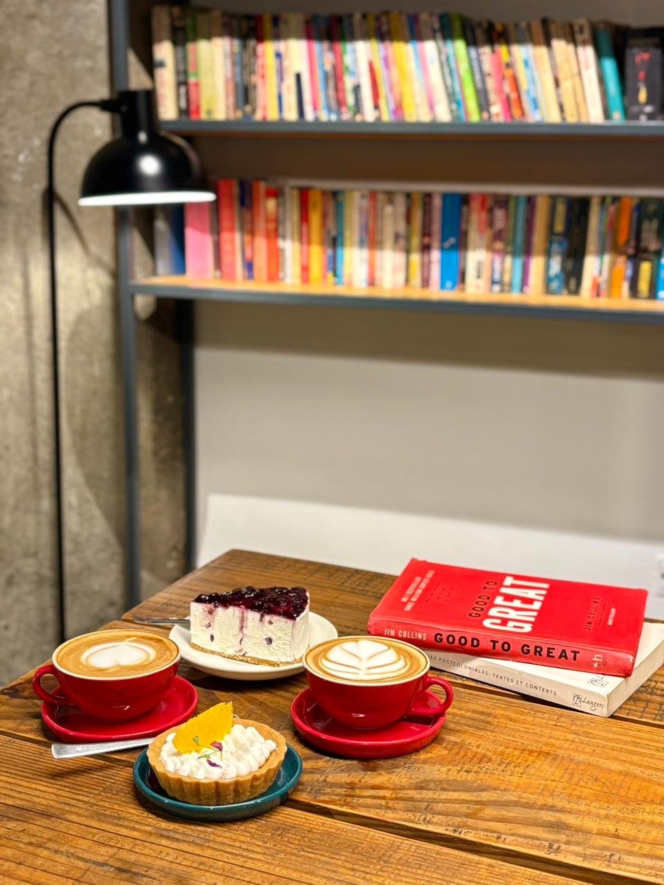 Two lattes, cheesecake and a tart by a wall of books