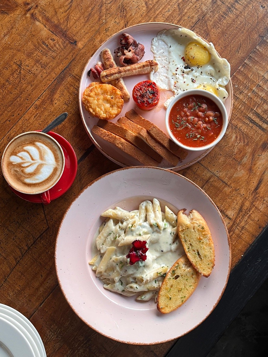 Cheesy alfredo penne with garlic bread next to a full breakfast and a latte