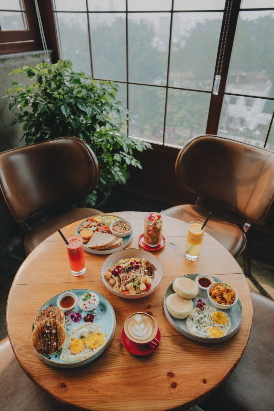 A table spread with breakfast plates, latte, and fresh juices by the window