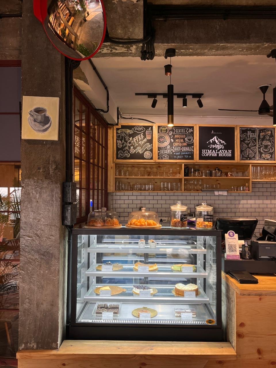 Coffee counter with chalkboard menus, glass cake display and the Himalayan Coffee House sign