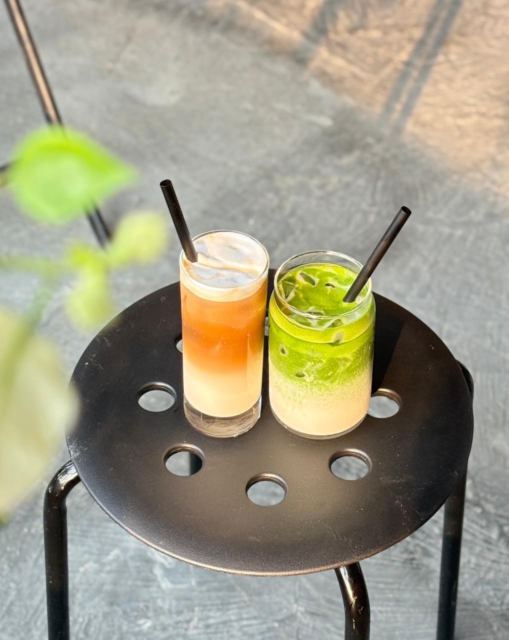 Layered iced coffee and iced matcha latte on a black stool