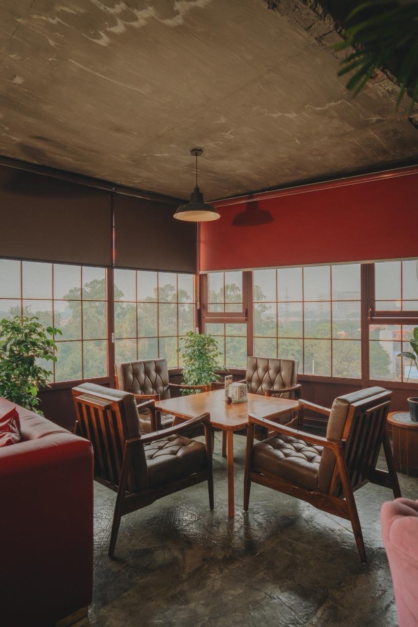 Tufted leather chairs around a table under a red wall and windows