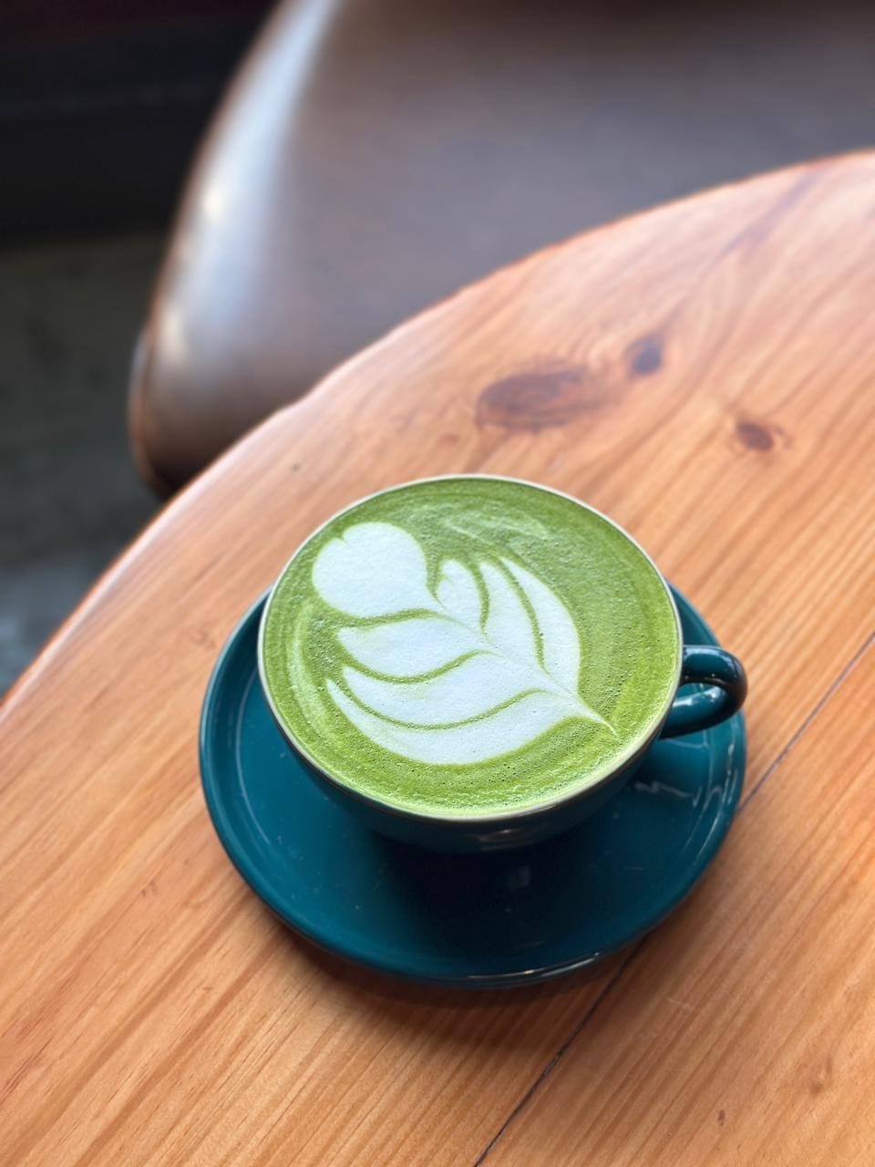 Matcha latte with leaf latte art in a teal cup