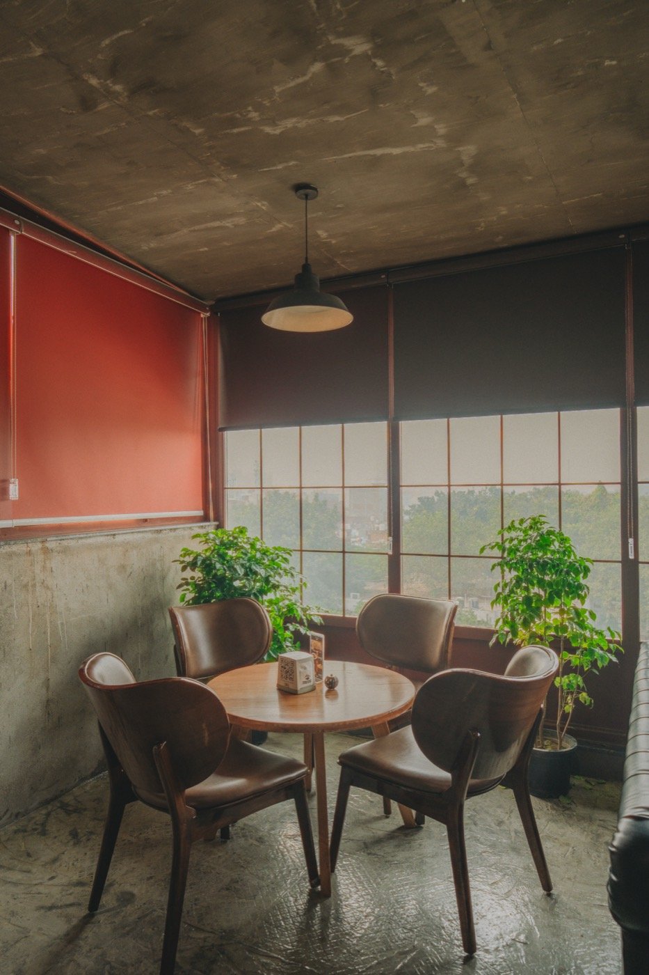 Round wooden table for four beside tall paned windows and potted plants